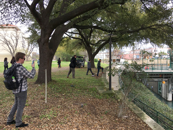 Students in the four IAH finalist teams explore the vegetated project site along the river. A bridge across the river is visible in the background. 