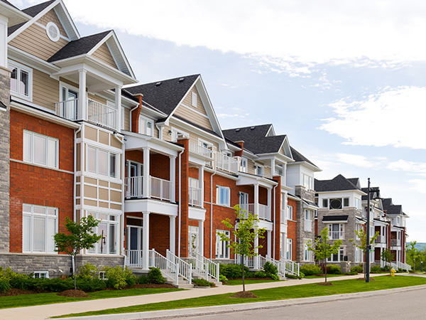 Multistory multifamily residential buildings with facades of brick, stone, and siding line a sidewalk.