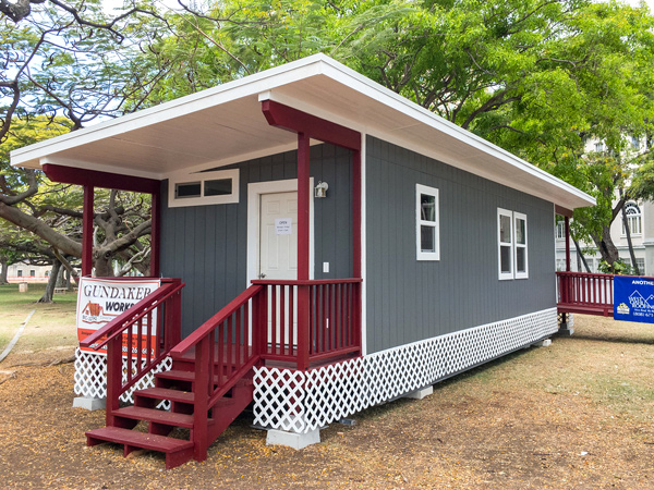 Photograph of a small, flat-roofed manufactured home on pilings in a yard, with front
door access via stairs and back access via a ramp.