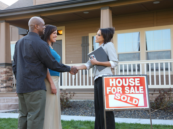 Photo of a couple shaking hands with a realtor outside a new house.