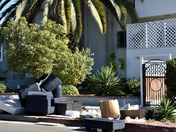 Photo of a house with discarded furniture strewn on the sidewalk in front of it.