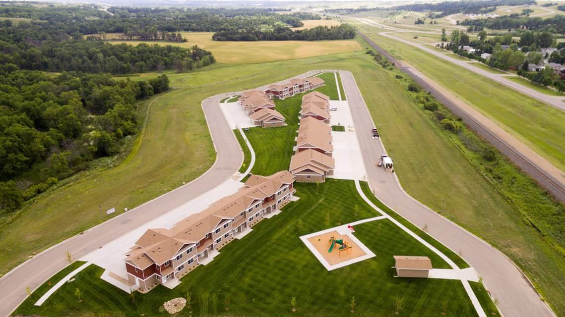 Aerial photograph of a development of four two-story buildings of five attached units each, with a children’s playground on-site. 