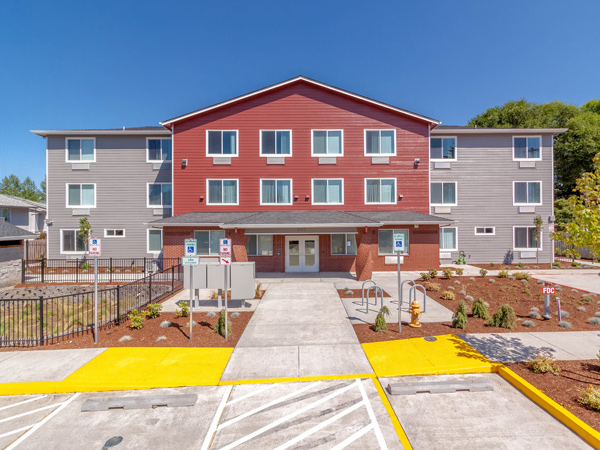 An image of a 3-story building with a wood and brick façade and a parking lot in the foreground.