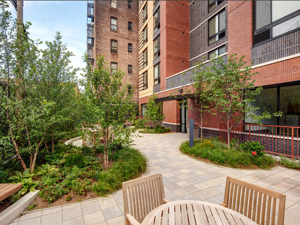 A seating area in front of a landscaped courtyard and multistory brick façade apartment building.