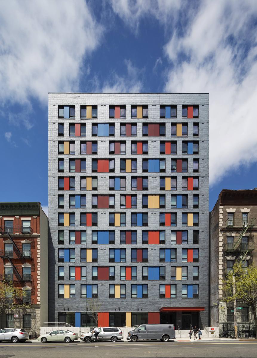 Photograph of the front façade of a 12-story apartment building, sitting between two buildings of approximately half of its height.