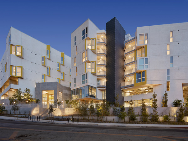 A photograph of two multi-story buildings connected at the ground level with a tree-lined sidewalk in the foreground.