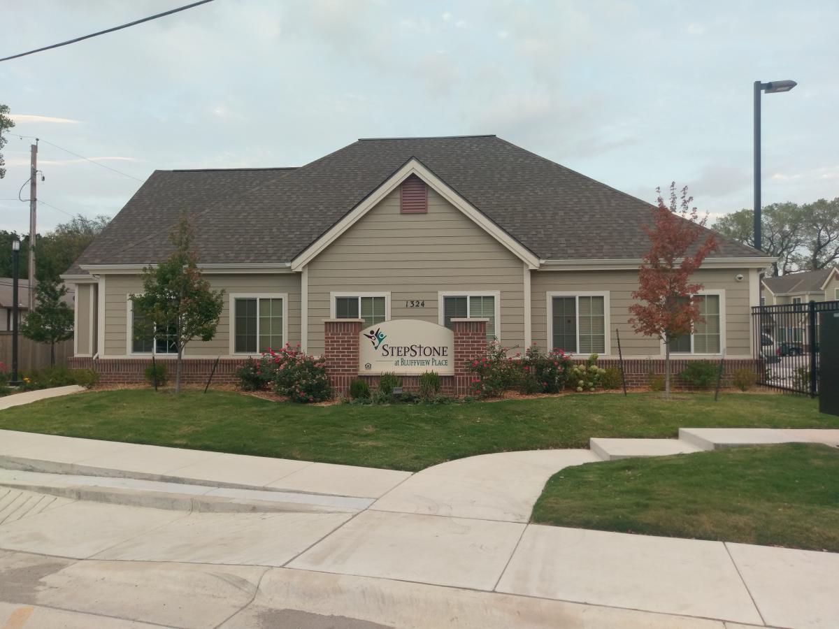 Photograph of the front façade of a one story building surrounded by a lawn, with a sign that reads “StepStone at Bluffview Place” in front.