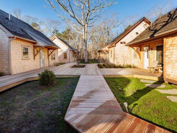 Image of cedar-shingled Cape Cod-style homes surrounding a shared wooden deck. Image of cedar-shingled Cape Cod-style homes surrounding a shared wooden deck.