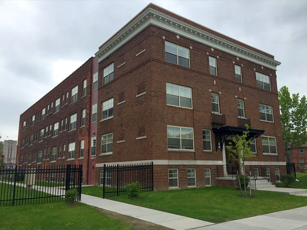 Photograph of the front and side façades of a multi-story brick residential building, with a stair entryway connecting to the sidewalk.