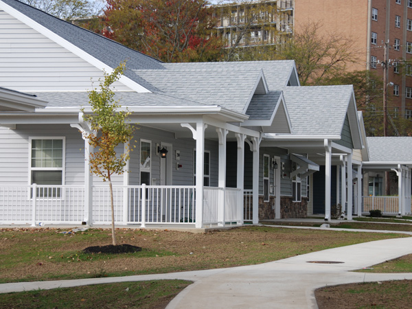 Photograph of the front and side facades of three single-story detached houses with front porches, each connected by a concrete path.