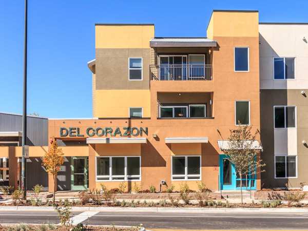 Image of a three-story apartment building taken from ground level, with the name “Del Corazon” over the entrance.