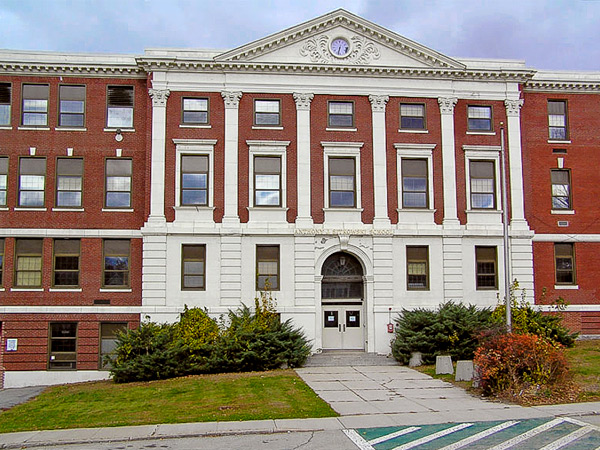 Photograph of the front façade of a large red brick four-story building with a white pilasters flanking the entrance.