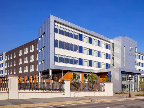 Five-story building facing street with sidewalk, trees, and light post in front.