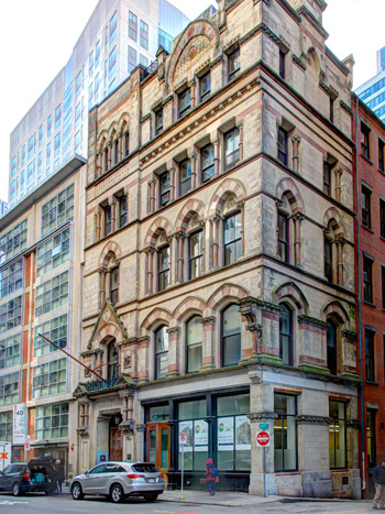 Image of a five-story Gothic style building with two cars parked in front.