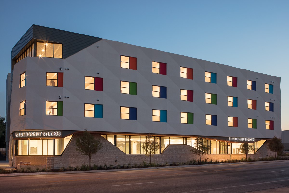 Photograph of the front façade of a four-story apartment building with multicolored window panels representing different apartments.