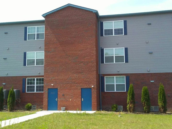 Photograph of a three-story apartment building with brick on the first level and windows flanked by shutters throughout.