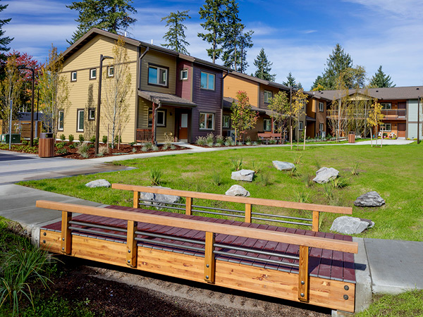 A bridged walkway in front of a large green space surrounded by two-story buildings.