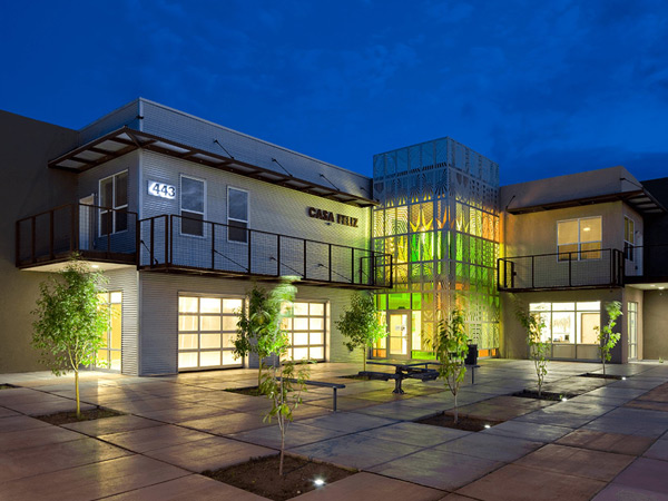 Photograph of an L-shaped, two-story community building taken across a courtyard planted with fruit tree saplings.