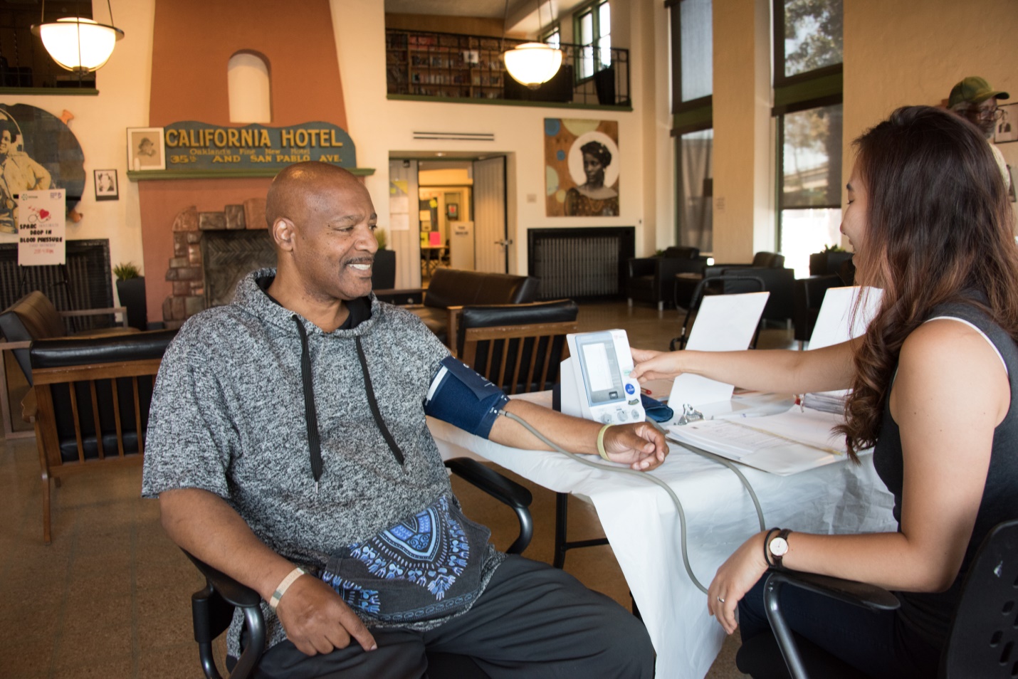 A man receives a blood pressure screening in a large, well-lit community space.  