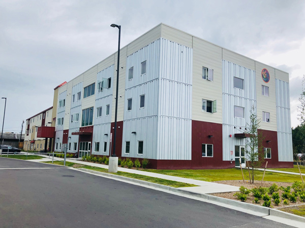 Image of a three story apartment building in the foreground, with an attached three-story residential structure in the background.