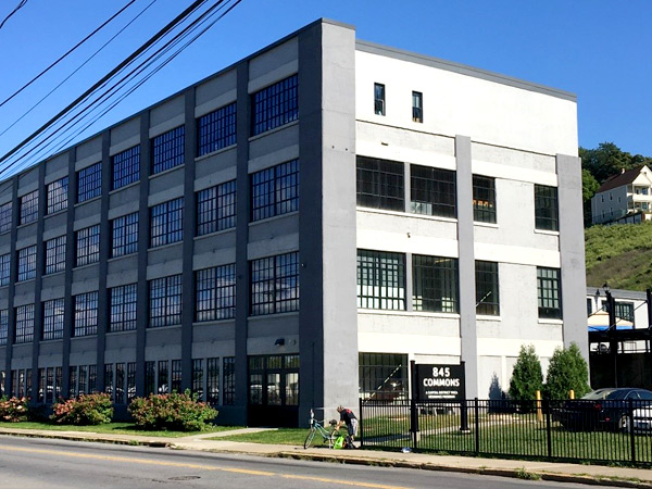 A four-story building with large glass windows and a sign in front that says “845 Commons.”