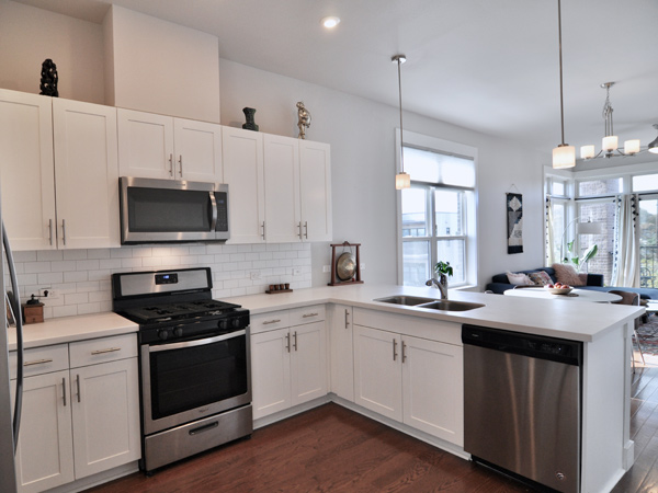 A condominium kitchen and living room with windows and furniture on a sunny day.