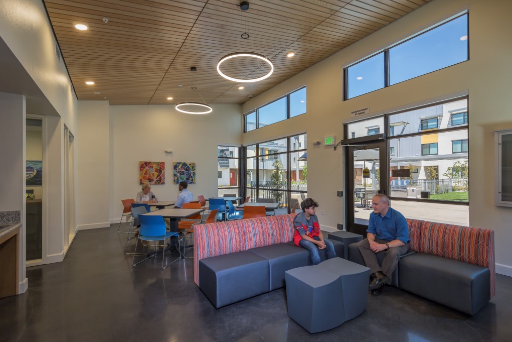 Photograph of a common area inside a building, with individuals seated on couches and chairs with tables.