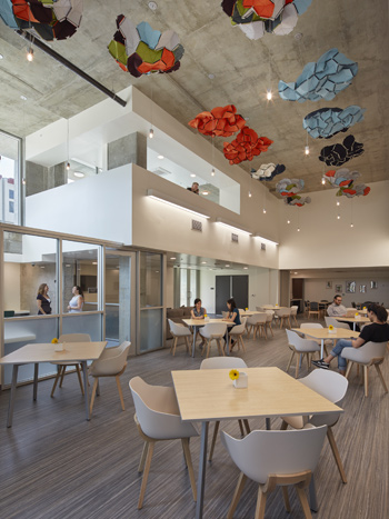 A photograph of a large room with high ceilings and several tables and chairs that has separate meeting rooms with windows along one wall.