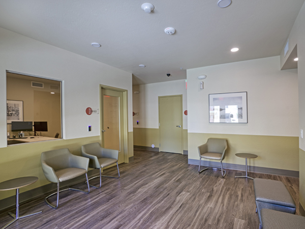 Photo of a room with seats and tables, with two computers behind a closed door in the background.