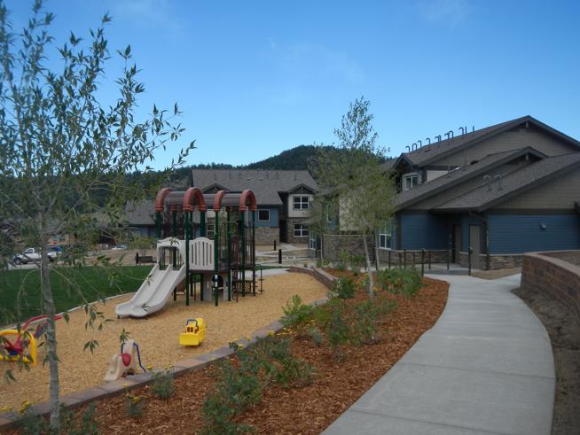 Photograph of a playground with slides and two two-story apartment buildings.