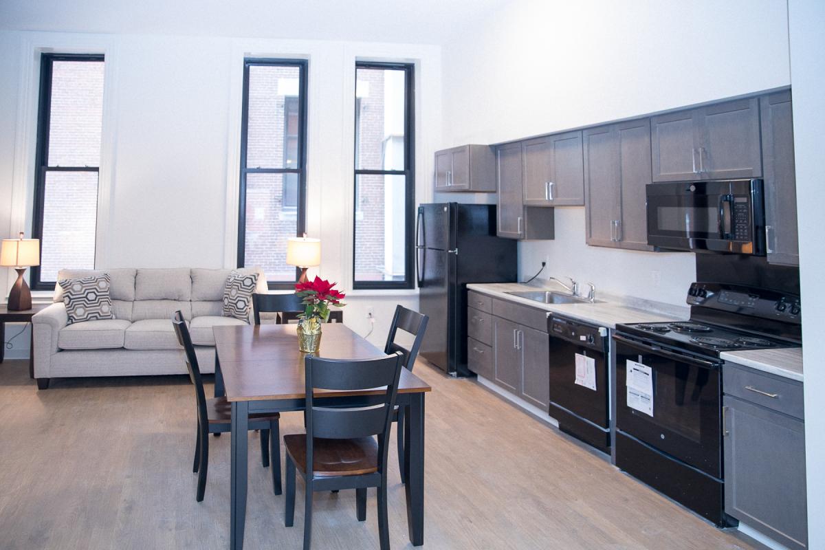 Image of an apartment interior furnished with a kitchen table, oven, dishwasher, refrigerator, and sofa.
