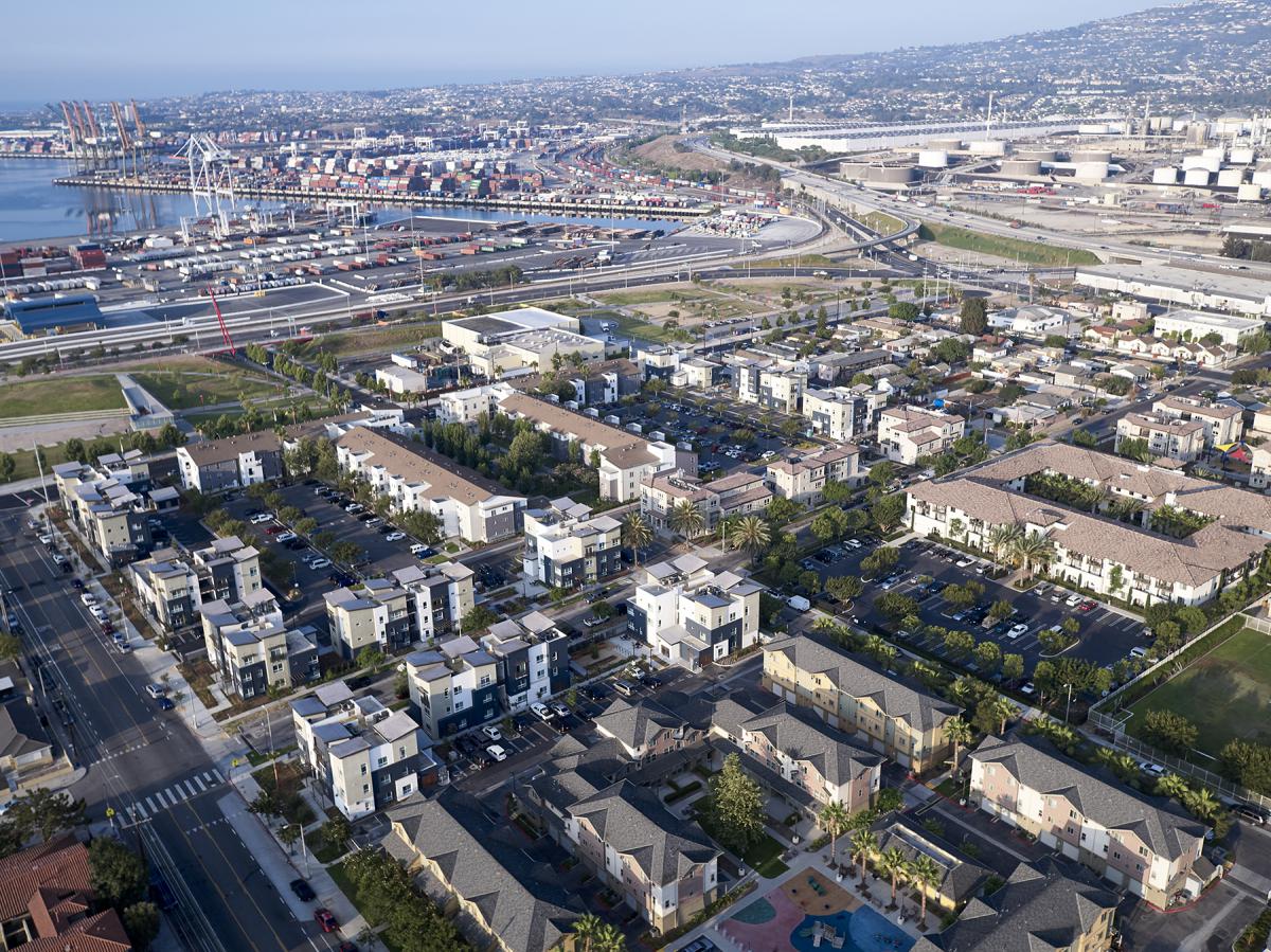 Aerial photograph of a portside neighborhood of primarily multifamily housing, interspersed with greenspace, parking, and a children’s play area in the foreground.