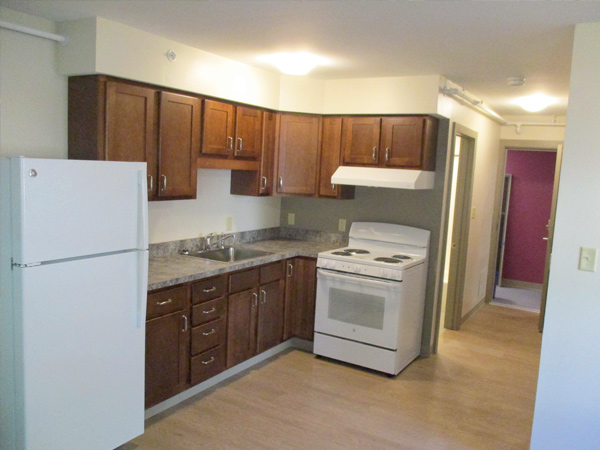 An apartment kitchen with a refrigerator, cabinets, countertops, sink, and oven.