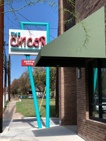 A bright-colored vertical sign for a commercial and residential building in a city neighborhood.