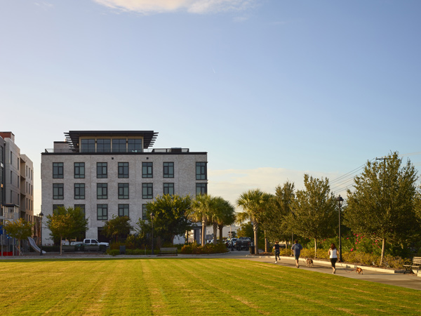 Picture of a four story apartment building behind an open, grassy park.