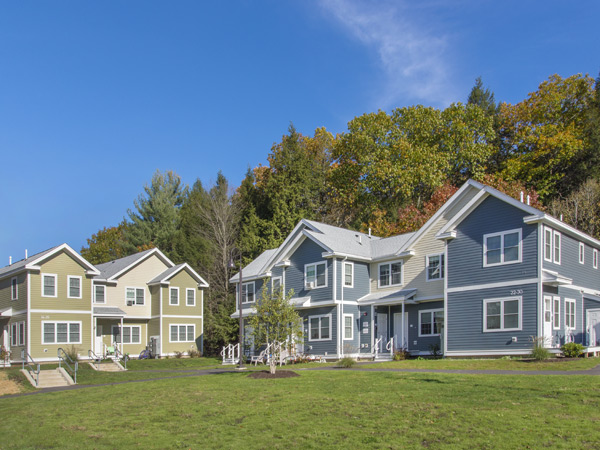 Photograph of two multistory, colonial-style apartment buildings, with a field visible in the foreground and trees shown in the background.