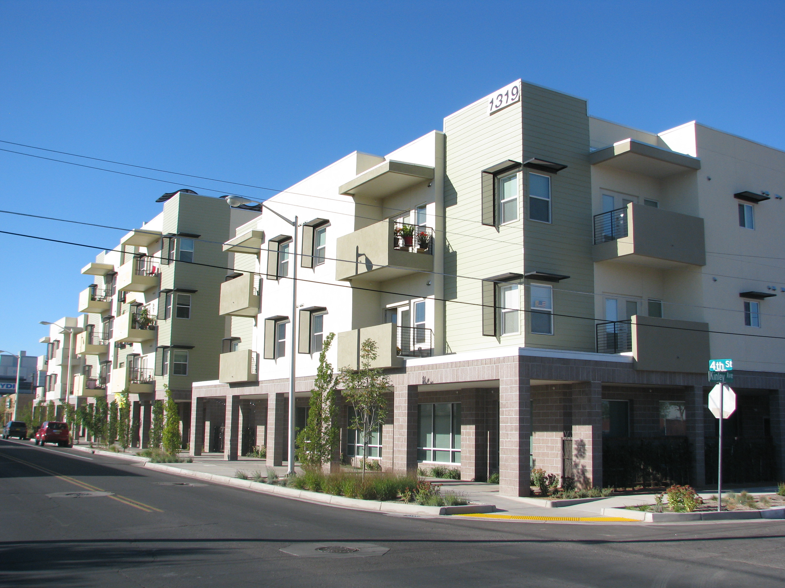 Photograph of a three-story apartment building on the corner of a street with a colonnade above the sidewalk.