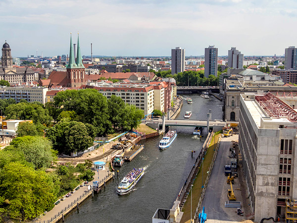 Arial photograph of a river, crossed by bridges and surrounded by greenery, near Berlin's city center.