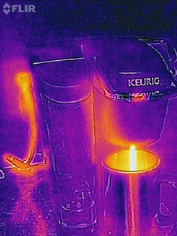 A Thermal image of a coffee machine pouring coffee into a mug, in which the heat flowing through the electrical cord and the coffee are visible.