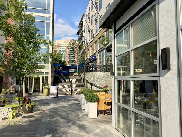 Photograph of an outdoor seating area and walkway in between multi-story buildings.