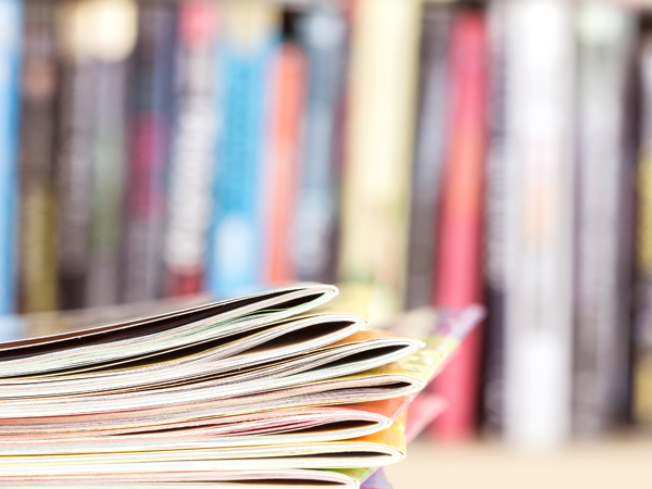 A stack of publications on a table with shelf of publications visible in the background