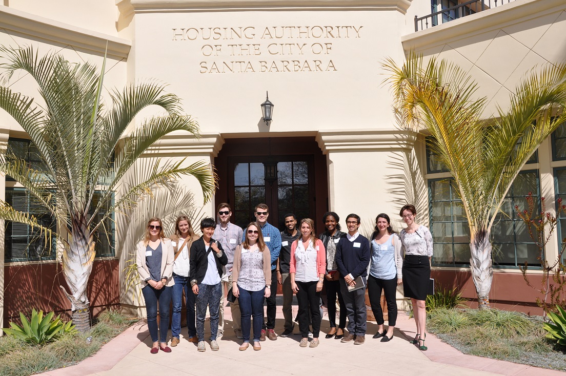 Image of twelve individuals standing in front of a building inscribed with the words “Housing Authority of the City of Santa Barbara” and flanked by palm trees.