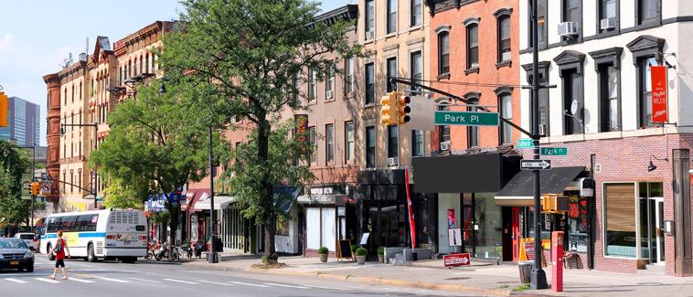 Photograph of a street corner at the intersection of Park Place and Flatbush Avenue in the Prospect Heights neighborhood in Brooklyn featuring the facades of several contiguous mixed-use buildings.