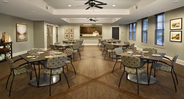 Photograph of a large multi-purpose room with a wooden floor and six tables set for dining. 