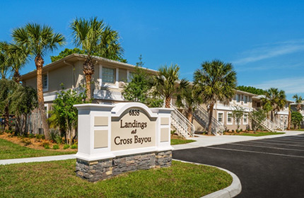 Photograph of several two-story residential buildings with a freestanding sign in the foreground reading "Landings at Cross Bayou."