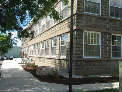Photograph of a two-story building with a stone façade and a bicycle rack and access ramp near the entrance.