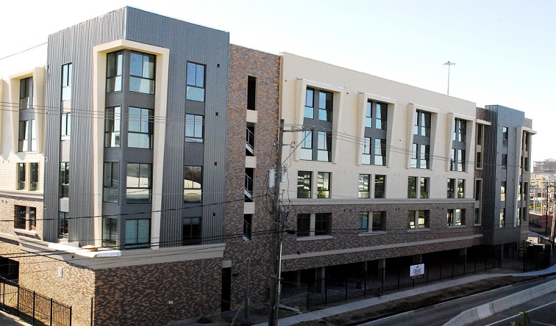 Photograph of a five-story brick, metal, and vinyl-sided apartment building with a garage on the ground level.