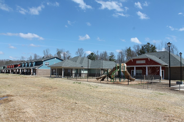 Photograph of a gazebo and picnic area with a community building and townhouses in the background.