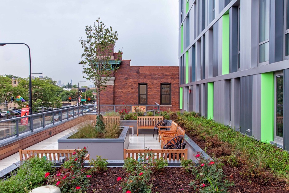 Photograph of a garden terrace with several benches on the roof of the single-story section at the front of the new apartment building.