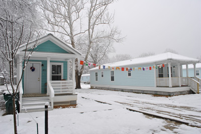 Photograph of two narrow one-story residences with a front porch and wood siding.